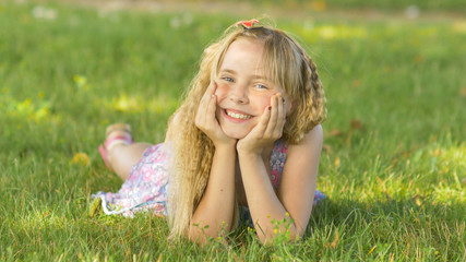 Beautiful young blonde girl lying on a field, green grass. Outdoors Enjoy Nature. Healthy Smiling...