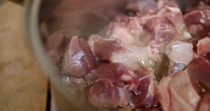 Pieces of raw lamb in boiling oil sliding