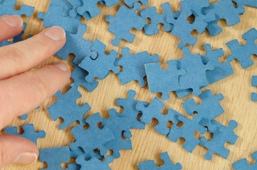 hand sorting through blue jigsaw puzzle pieces on wooden background