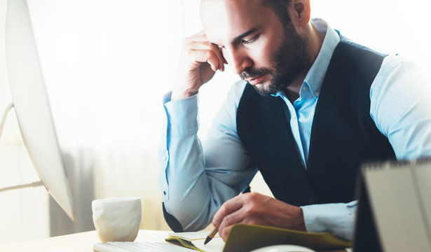 Bearded businessman working on modern office. Consultant man thinking looking in monitor computer. Manager writes in notebook in coworking workplace, startup project concept in studio with coffee