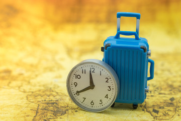 Time and Travel concept. Close up of miniature blue baggage with vintage round clock on world map.
