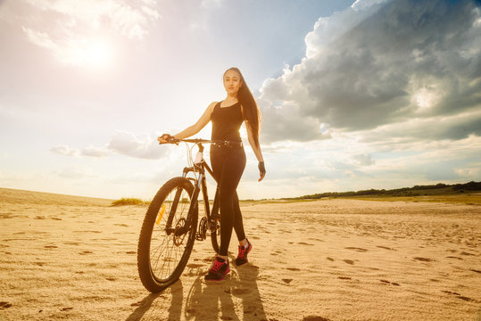 Bicyclist the summer sunset on the desert road in the reserve territory. Full length image of young female cyclist. Summer sunset. Bicycle and ecology lifestyle concept.