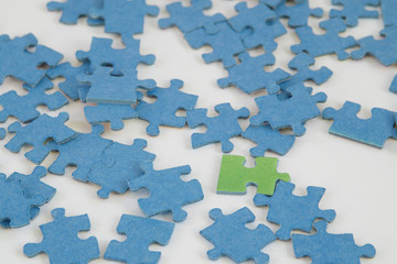 One green jigsaw puzzle piece between blue pieces, white background