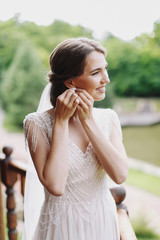 Wedding. Bride. Preparations. Wedding Dress. Happy bride in white lace dress wears the earring on the balcony