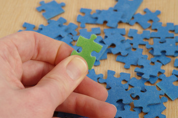 Hand holding one green jigsaw puzzle piece, blue and wooden background