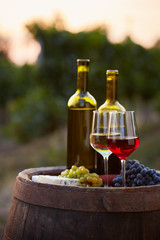 Fototapeta premium Pair of wine glasses and bottles on old barrel with bunch of grapes