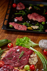 Still life of raw beef meat with vegetables on wooden plate, cooking tray over rustic background, selective focus