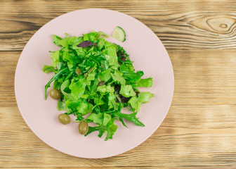 Obraz na płótnie Canvas Fresh lettuce leaves, basil, arugula in a glass bowl on a wooden background. Preparation of a vegetarian vegetable salad.