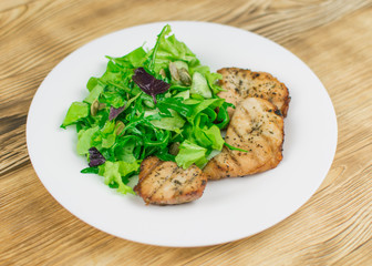 Salad of leaves and grilled meat on a wooden background.