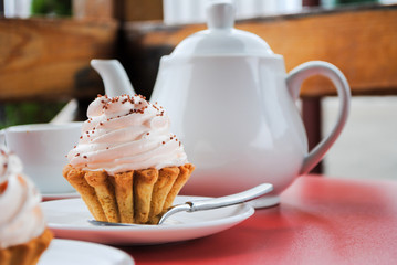 Appetizing cake with pink cream and sprinkling on a table with a teapot and cups for tea.