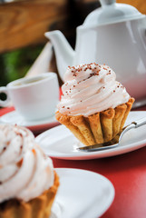 Appetizing cake with pink cream and sprinkling on a table with a teapot and cups for tea.
