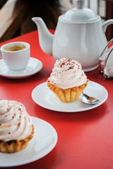 Appetizing cake with pink cream and sprinkling on a table with a teapot and cups for tea.