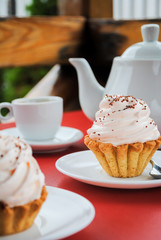 Appetizing cake with pink cream and sprinkling on a table with a teapot and cups for tea.