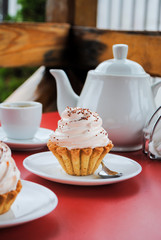 Appetizing cake with pink cream and sprinkling on a table with a teapot and cups for tea.