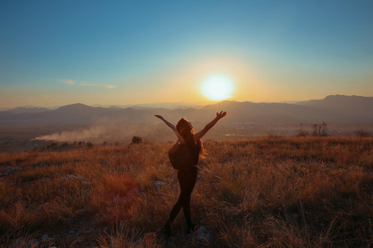 Sunset mountain. Tourist Free happy  woman outstretched arms with backpack enjoying life in wheat field. Hiker cheering elated and blissful with arms raised