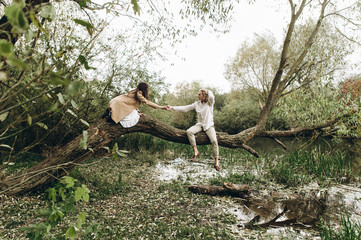 A beautiful couple in the boo style embraces sitting on a branch over the lake
