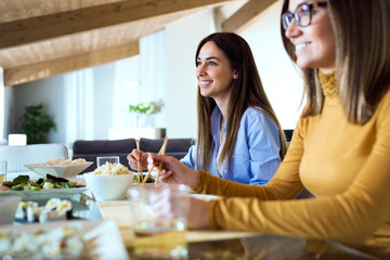 Two beautiful young women eating japanese food at home.