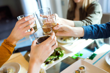 Four young women toasting with wine while eating at home.