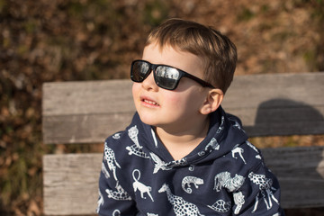 Trendy little boy in sunglasses looking up.Outdoors