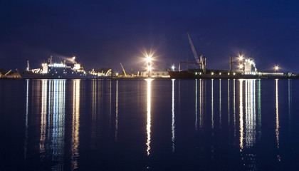 Ships in the port of bakaritza in the light of night lights. Arkhangelsk. Pillars of light reflected in the water