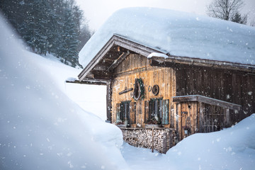 Snowflakes in foreground, old traditional wooden cabin lodge shack in bavarian alps with lots of...