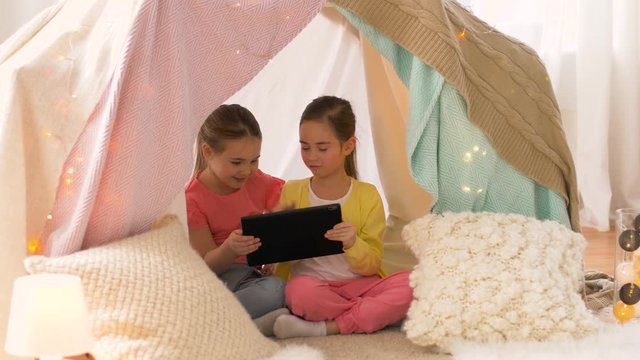 childhood, friendship and technology concept - happy girls with tablet pc computer in kids tent or teepee at home