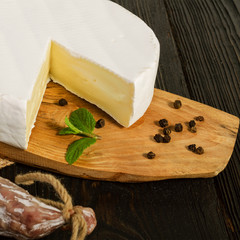 Round Camembert cheese, sliced, on a wooden board and fuet sausage, on a wooden board, with sack.