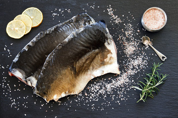 Close-up photo of fresh raw fish fillet with sea salt and lemon on black concreted table background