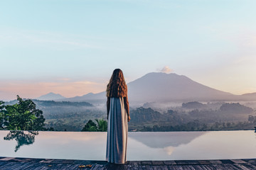 beautiful girl staying near swimming pool with fantastic volcano Agung view