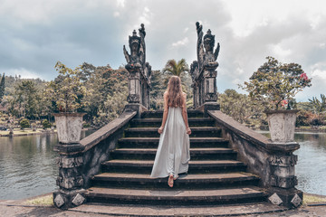 beautiful girl with long dark hair in elegant grey dress posing on old bridge in Tirta Gangga