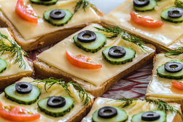 Smiling sandwiches with face from cucumbers, tomato, olive and dill. Perspective view with limited depth of field.