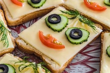 Cheese sandwich with face from cucumbers, tomato, olives and dill