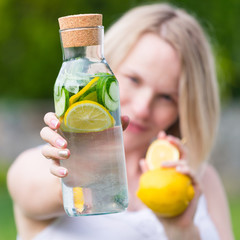 healthy eating, drinks, diet. The girl is holding a detox drink from a lemon and mint with a cucumber on a background of green grass