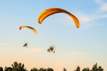 Flight of two motor paragliders trike skyward. Flight on motor gliders in the blue sky over the green trees.