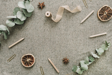 Frame of eucalyptus branches, pencils, dry oranges on beige blanket background. Flat lay, top view rustic mock up. Wedding festive minimal concept.
