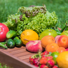Various vegetables and fruits on a wooden tray against a background of green grass