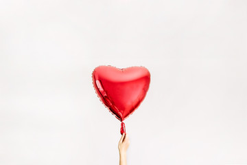 Women's hand holding red heart shape balloon. Love concept.