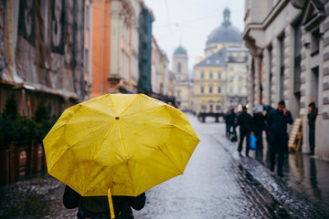 woman walk by old european streets in rainy weather with yellow umbrella. copy space