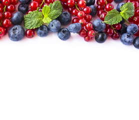 Mix berries and fruits at border of image with copy space for text. Ripe blueberries, blackberries, strawberries, currants and strawberries on white background. Top view. Black-blue and red food.
