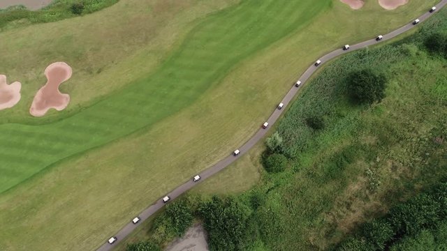 drone top shot of golf carts travelling in a line on a winding golf course