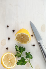 one lemon cut in half with a metal knife and a leaf of greens on white background. Top view. Flat lay. Copyspace