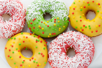 Pink, Yellow, Green Donuts with  red, green polka dots on a white plate close-up. National Doughnut Day. Fried dough confectionery. Snacks. Dessert food.