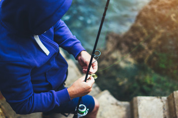 young man holds a fishing rod and catches fish in the nature on a sea background, hipster fisherman spends vacation on ocean, active travel hobby fishing, rural outdoor sport tourism, top view
