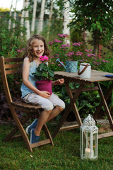 happy kid girl playing in summer garden, holding heranium flower in pot. Teaching kids to love nature and take care about plants