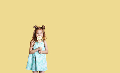 Portrait of a beautiful smiling little girl. Girl with big sweets on a yellow background with copy space