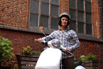 Handsome man wearing casual clothes in a helmet, riding on a retro classic scooter, along the old streets in a Europe.
