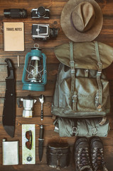 Camping stuff arranged on wooden backdrop. Machete, boots, lantern, camera, hat, map, compass....