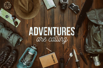 Adventures are calling text, message, lettering. Hiking gear frame including machete, knife, clothes, boots, lantern, notepad, hat, map, compass. Wanderlust postcard, poster, banner.