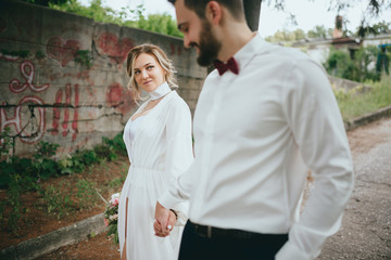 Happy newlywed couple on a walk in old European town street, gorgeous bride in white wedding dress together with handsome groom