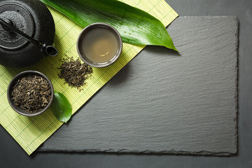 Green japanese tea on black slate background. Black teapot and bowl with green tea. Top view with...